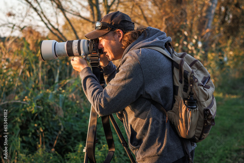 Man photographer with camera on tripod is taking picture of nature in forest
