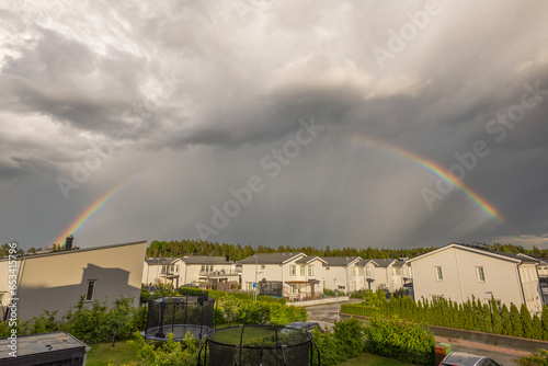 Beautiful panoramic view of rainbow above modern village with white houses. Sweden.