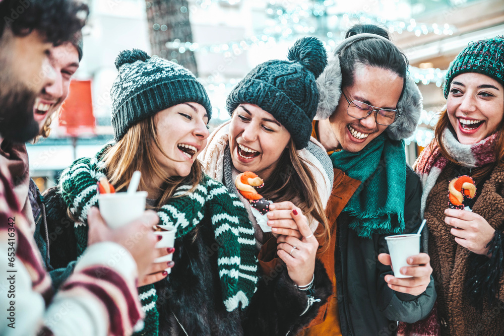 Obraz premium Happy friends having fun drinking mulled wine and hot chocolate at Christmas Market - Cheerful young people enjoying winter holidays on weekend vacation - Tourism lifestyle and friendship concept