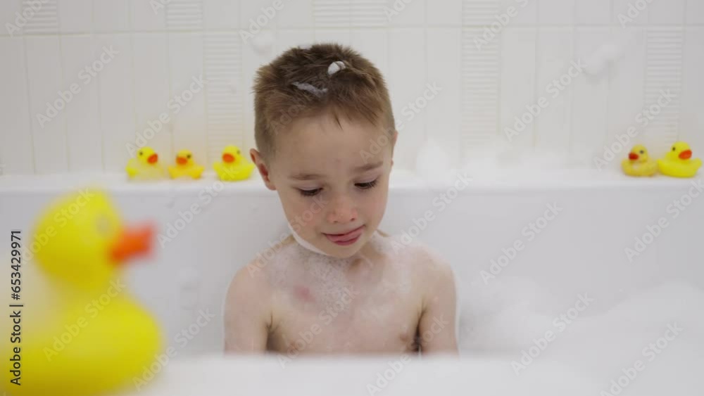 Little child sitting in bath filled with foam, playing with toys in bath and smiling Little child sitting in bath filled with foam, playing with toys in bath and smiling