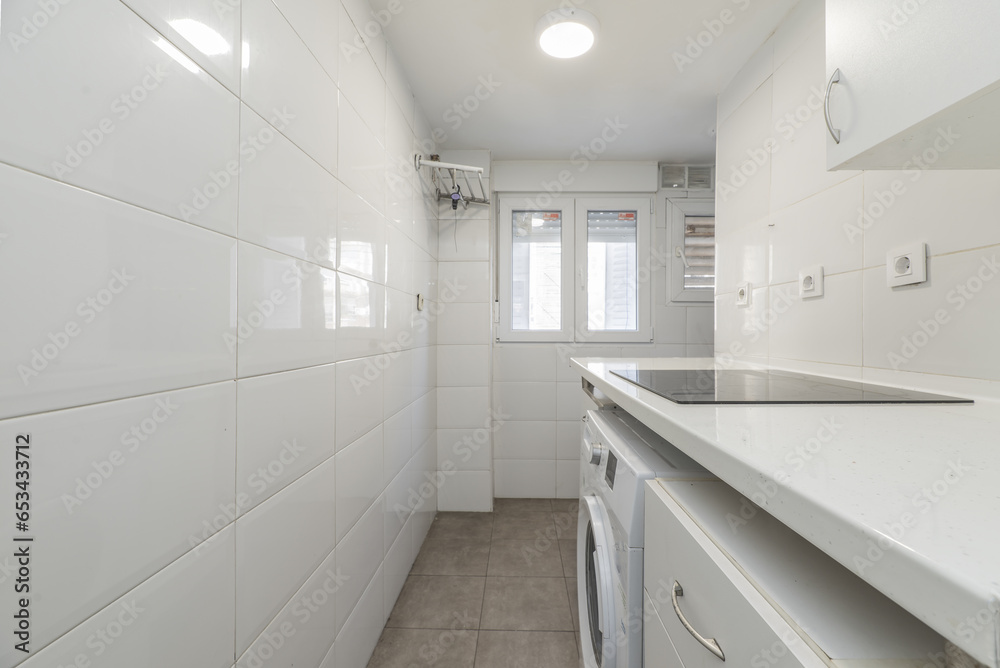 Image of a small kitchen furnished with white wooden furniture and countertops of the same color with integrated white appliances and aluminum window