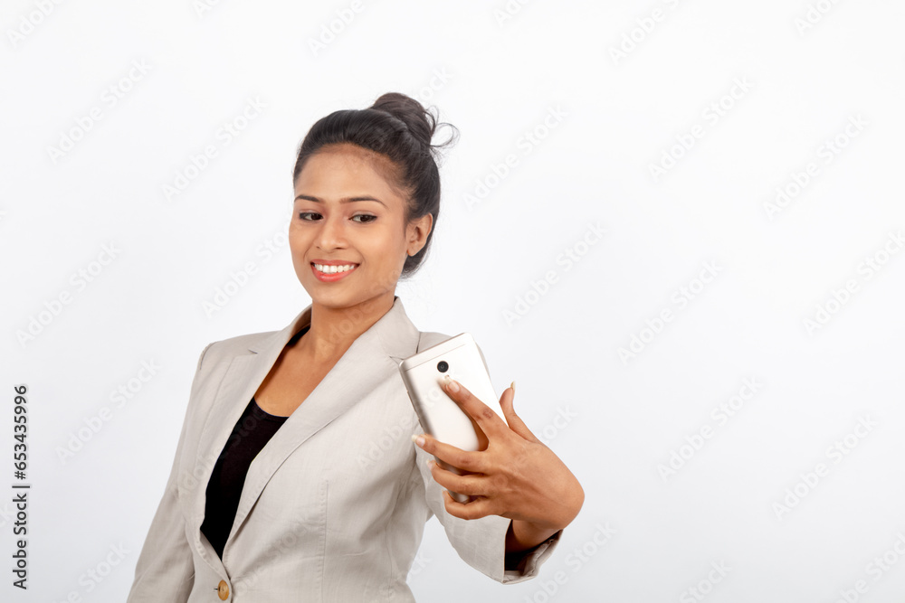 Corporate office lady with black hair having playful moment with smart phone in formal wear wearing white blazer against white background. Corporate office lady with black hair having playful moment with smart phone in formal wear wearing white blazer against white background.