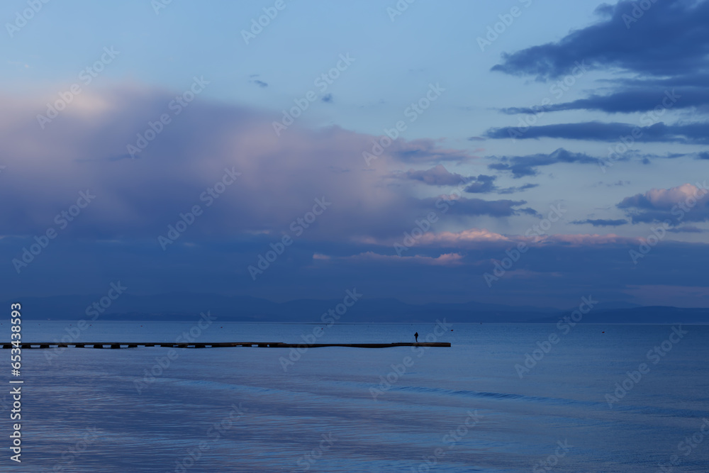 Person staying on pier or dock during a sunset over a sea