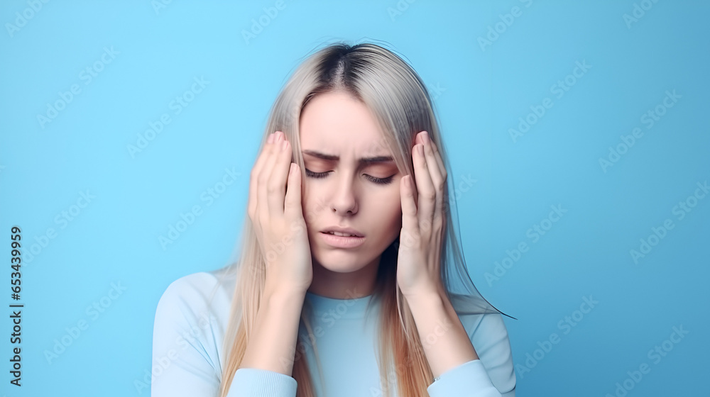 A girl is holding her head with severe migraine pain at blue background A girl is holding her head with severe migraine pain at blue background