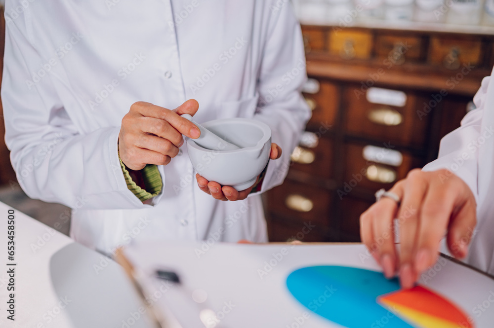 Obraz premium Pharmacists hands mixing cure in a mortar and holding a clipboard with cure ingredients