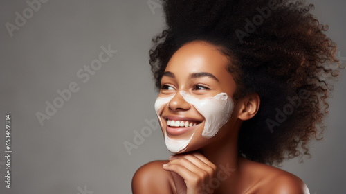 Smiling african american woman in grey background Enjoying. Applying face cream for skin care rutine. Copy space photo