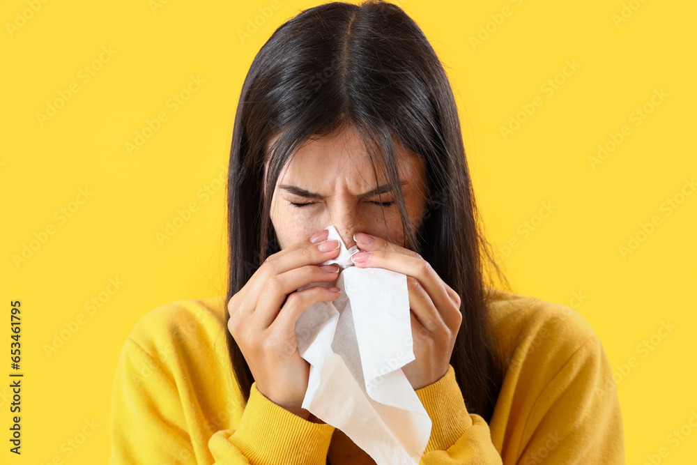 Allergic young woman with tissue sneezing on yellow background, closeup Allergic young woman with tissue sneezing on yellow background, closeup