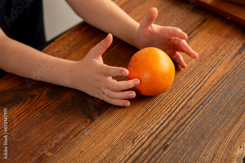 childish hands holding an orange over the table photo