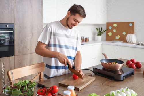 Young man cutting tomato in kitchen