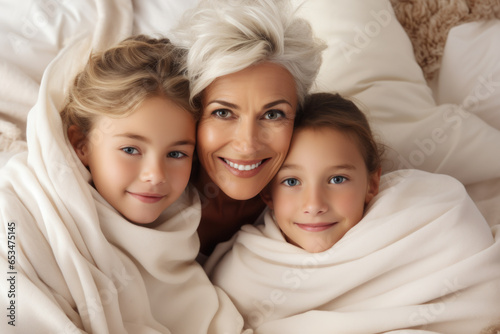 Woman is seen with two children, all wrapped up in warm blankets. This image can be used to depict cozy family moment or importance of staying warm during cold weather