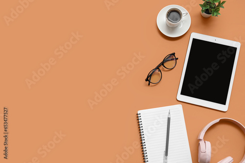 Tablet, cup of coffee and stationery on brown background