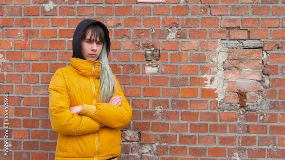 Stressed teen by brick wall. An offended sad young girl stand by the bricks wall in the day light. Stressed teen by brick wall. An offended sad young girl stand by the bricks wall in the day light.
