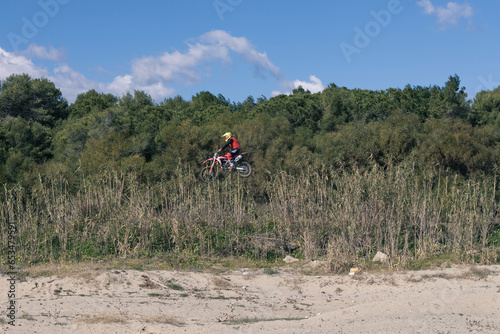 Photo of a motocross while it is flying in the middle of nature 