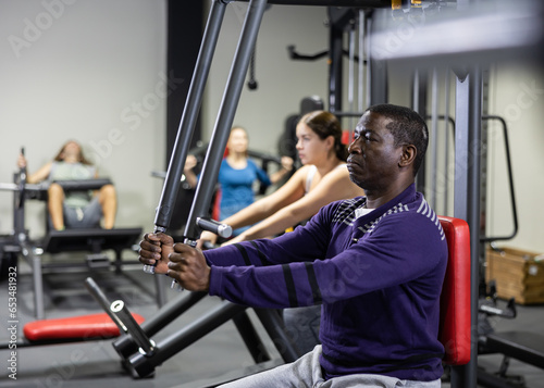 African-american man training on chest fly machine in gym photo