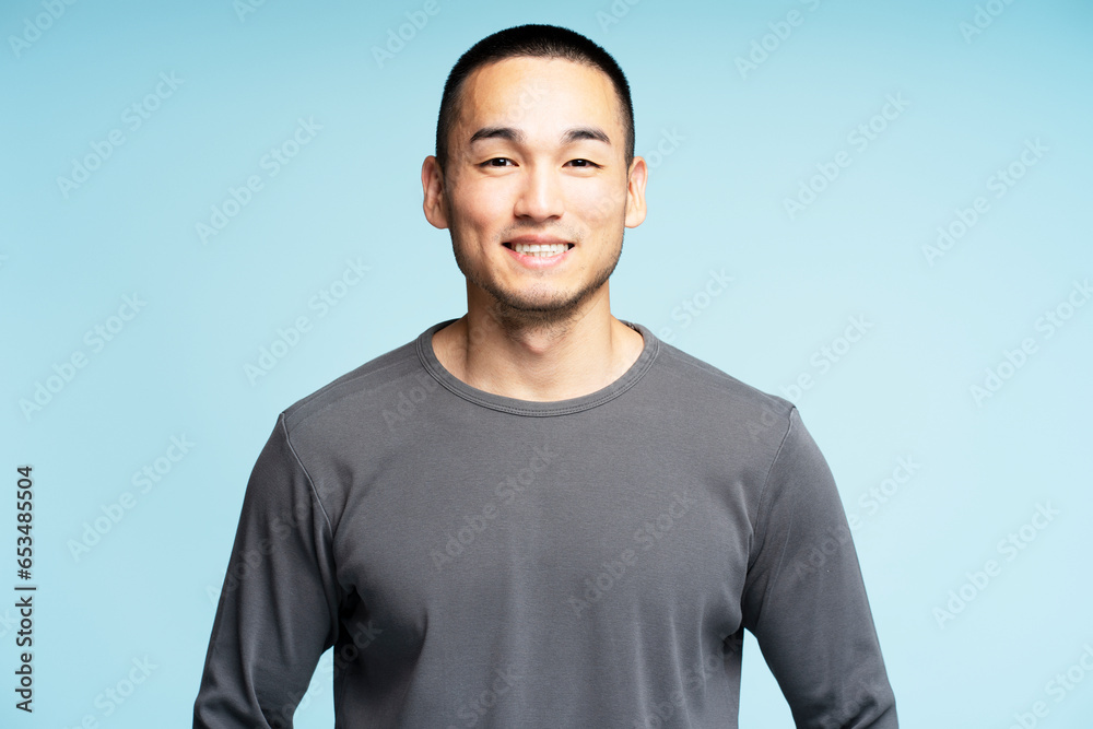 Portrait of smiling Asian man in casual clothes posing looking at camera isolated on blue background Portrait of smiling Asian man in casual clothes posing looking at camera isolated on blue background