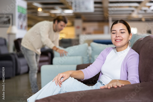 young woman in furniture store enjoys comfort of stylish armchair before making purchase
