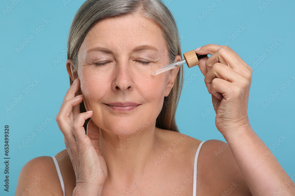 Senior woman applying cosmetic product on her aging skin against light blue background. Rejuvenation treatment Senior woman applying cosmetic product on her aging skin against light blue background. Rejuvenation treatment