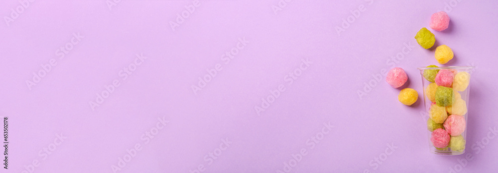 Plastic cup with color cotton balls on violet background, top view. Banner design with space for text