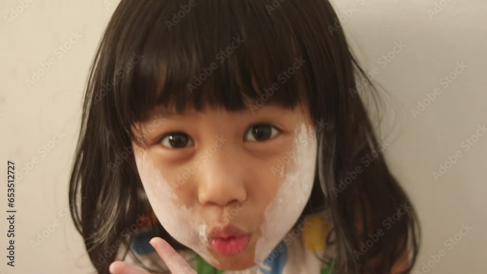 Little Asian baby girl playing with facial powder, blowing white powder on her face, close up Little Asian baby girl playing with facial powder, blowing white powder on her face, close up
