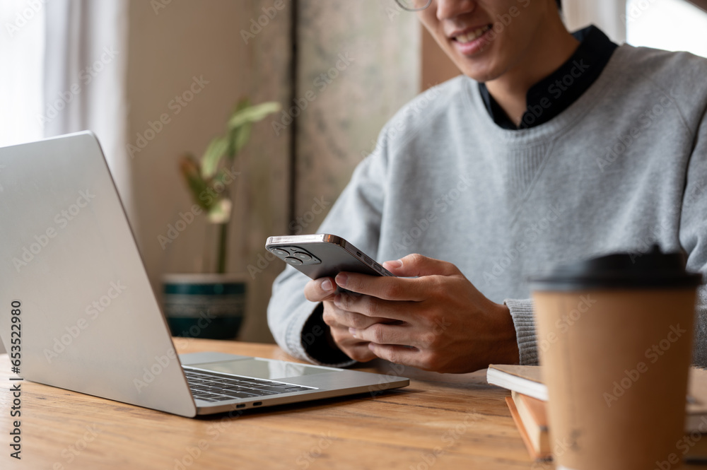 Close-up image of a handsome Asian man using his smartphone while working remotely at a coffee shop. Close-up image of a handsome Asian man using his smartphone while working remotely at a coffee shop.