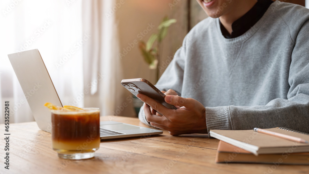 A happy Asian man enjoys chatting with his friends on his phone while working remotely at a cafe. A happy Asian man enjoys chatting with his friends on his phone while working remotely at a cafe.
