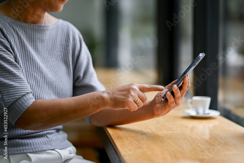 Close-up image of a retired lady is using her smartphone at a table while relaxing in a coffee shop.