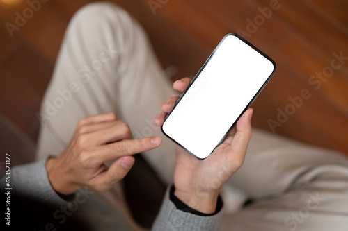 Close-up image of a man using his smartphone while sitting in a room. using app, texting, responding to messages © bongkarn