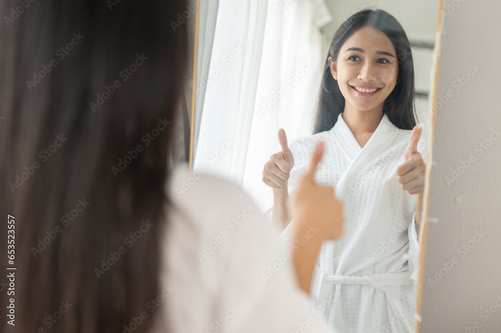 A confident woman in a bathrobe is smiling and giving herself a thumbs up in front of the mirror. A confident woman in a bathrobe is smiling and giving herself a thumbs up in front of the mirror.
