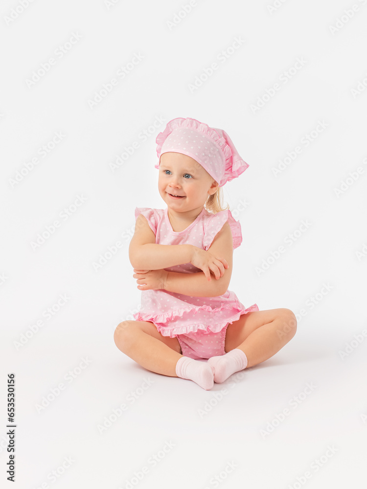 Satisfied, happy little girl 2 years old in a pink dress and a scarf sits on the floor, smiles playfully and hugs herself with her arms. Satisfied, happy little girl 2 years old in a pink dress and a scarf sits on the floor, smiles playfully and hugs herself with her arms.