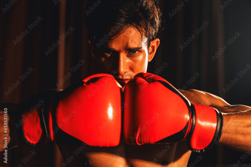 Φωτογραφία Muay Thai boxer punch fish his hand together in front of camera in ready to fight stance posing at gym with boxing equipment in background