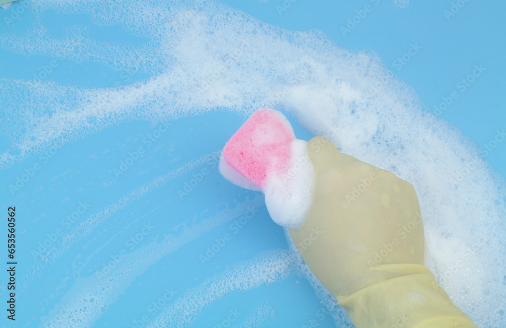 Fototapeta premium Human hand in protective glove with pink sponge in foam on blue background. 