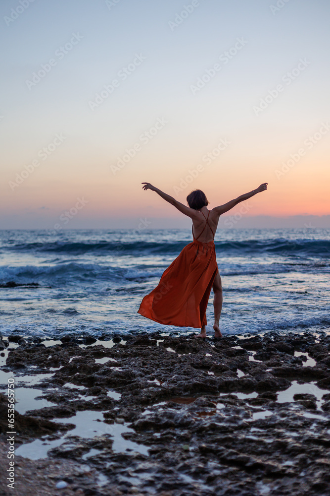 beautiful sensual woman in a red long dress posing on the seashore during sunset. beautiful sunset. beautiful sensual woman in a red long dress posing on the seashore during sunset. beautiful sunset.