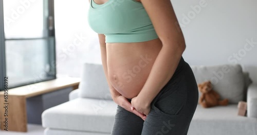Pregnant woman with incontinence and frequent urination during pregnancy. Pregnant woman need to pee standing by in Livingroom. Pregnancy concept video. Health and wellbeing of expectant mother. photo