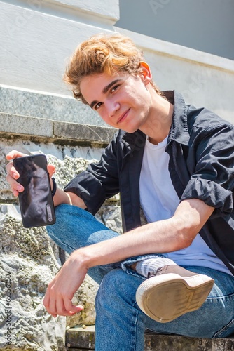 Image of a young Caucasian man smiling and holding a phone in his hand