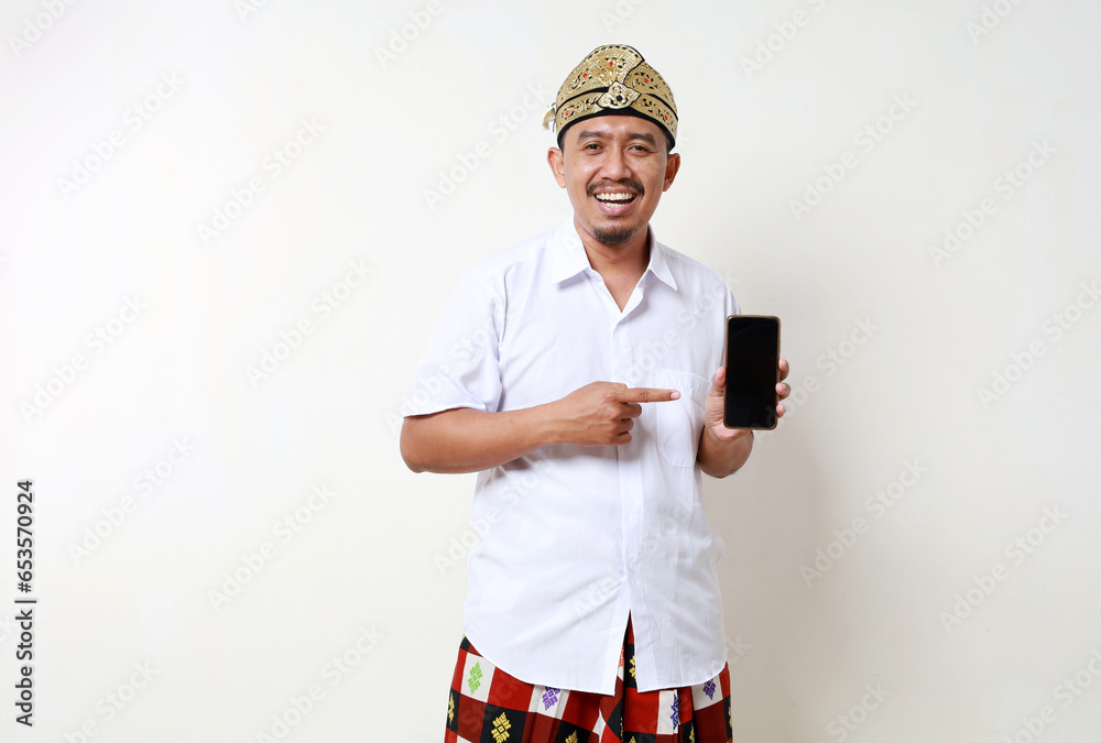 Excited Asian man in balinese traditional costume standing while showing a blank cell phone screen. Isolated on white background Excited Asian man in balinese traditional costume standing while showing a blank cell phone screen. Isolated on white background