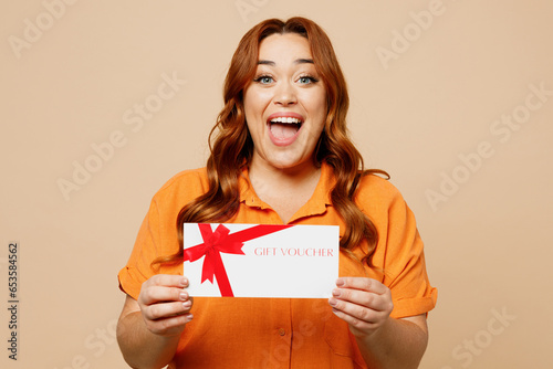 Tableau sur toile Young ginger chubby overweight woman wear orange shirt casual clothes hold gift certificate coupon voucher card for store isolated on plain pastel beige background studio portrait