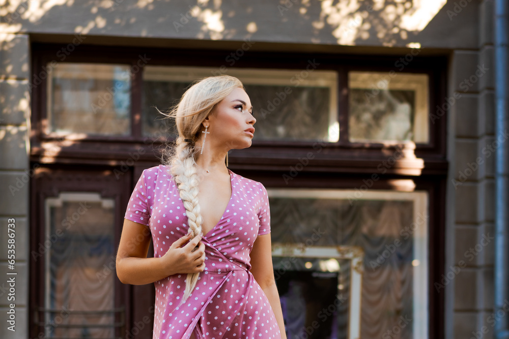 beautiful woman with long braid in pink dress with white polka dots posing on street in the city