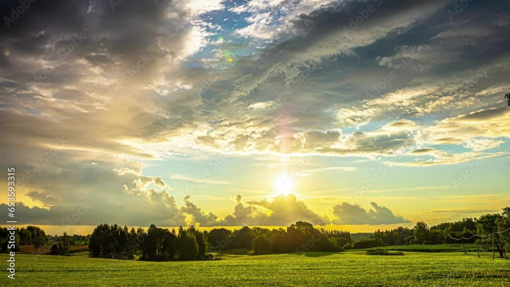 Timelapse shot of sun rising over green grasslands with dark clouds passing by at dawn.