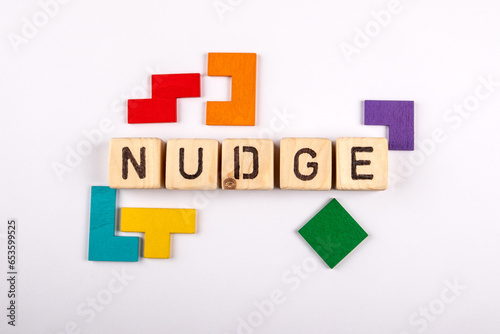 NUDGE. Wooden alphabet letters and colorful figures on a white background