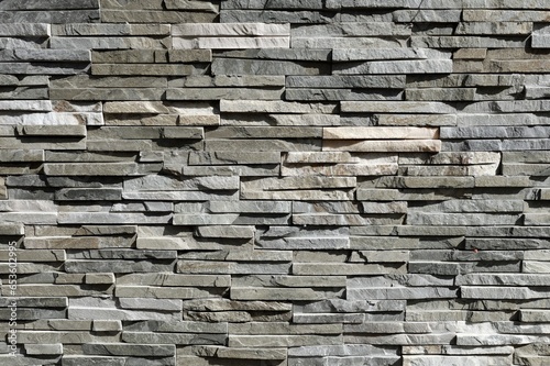 Stone cladding wall made of striped stacked slabs of natural gray and white rocks. Panels for exterior, background and texture. 