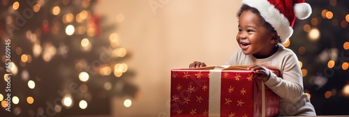 Banner Christmas Child opening present, portrait Happy African American baby Boy smiling in Santa Claus hat with giftbox at home near Chrestmas tree, copyspace.