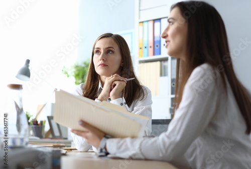 Portrait of smart businesspeople sitting in modern workplace and listening somebody with concentration. Gorgeous woman holding paper folder with charts and graphs. Accounting office concept