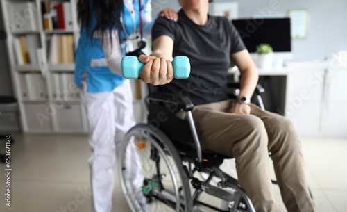 Close-up of patient in wheelchair at procedures of physiotherapist. Rehabilitation after injury. Doctor in uniform helping man. Healthcare and medicine concept