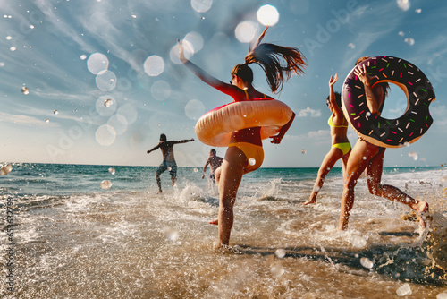 Old style photo of group of friends are having fun and running to sea beach with inflatable donuts