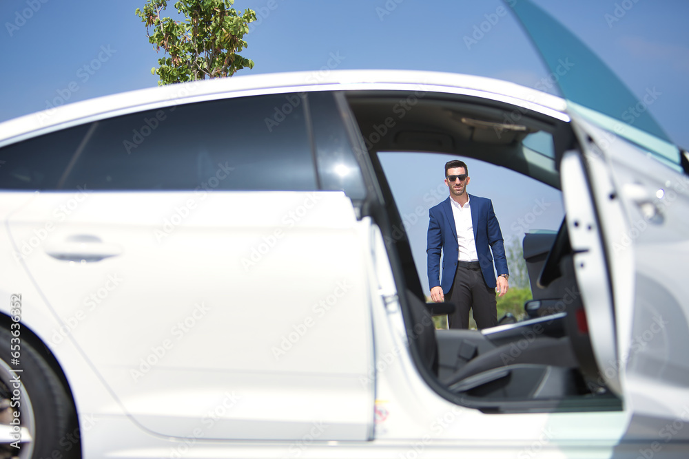 Successful, attractive, young Hispanic man in jacket and sunglasses seen through the open doors of his white luxury car. Concept, cars, luxury, success, businessman.