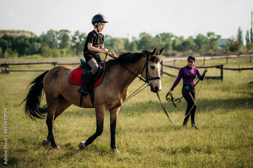 A teenage boy in a helmet learns horse riding in the summer, the instructor teaches the child equestrianism. A teenage boy in a helmet learns horse riding in the summer, the instructor teaches the child equestrianism.