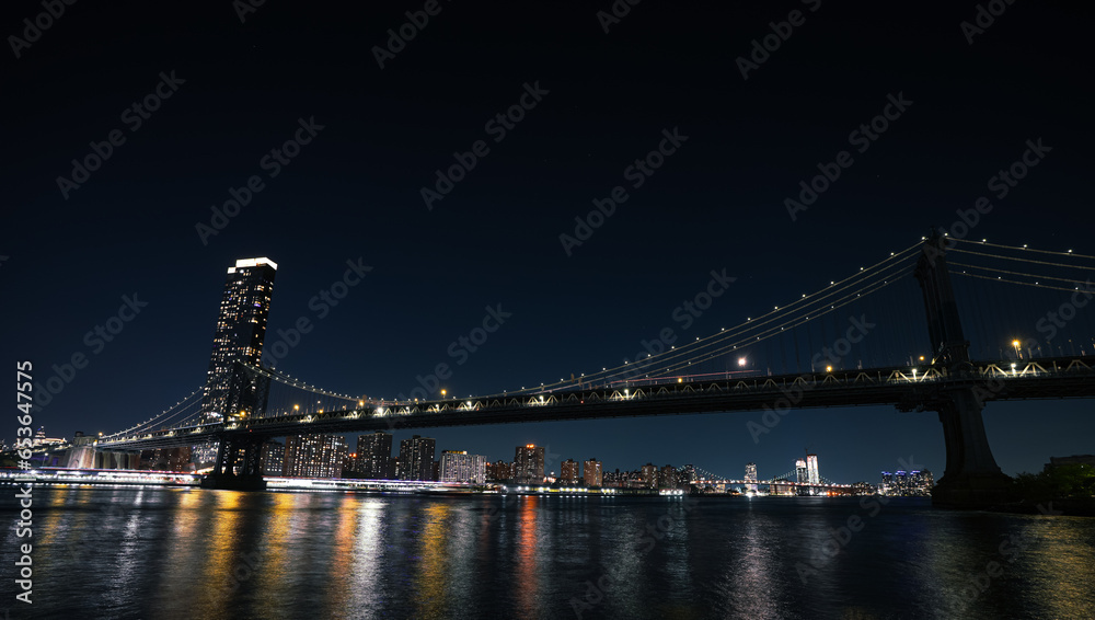 Fototapeta premium New York skyline by night. Landscape photo during the evening, view to Brooklyn and Manhattan bridge and landmark skyscraper office buildings from New York, America.