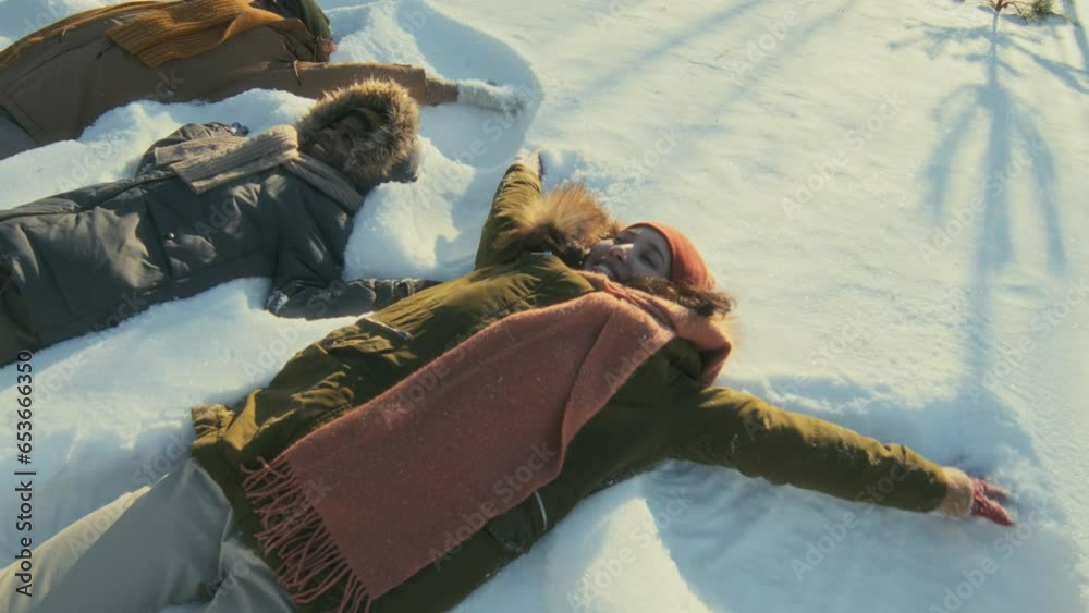 High angle view shot of cheerful ethnically diverse man, woman and their son lying on snowdrift making snow angels