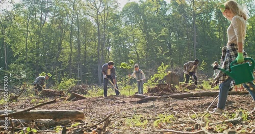 Side-view of beautiful caring father planting trees with little cute daughter. Enthusiastic family doing forestation work in forest and watering trees with other volunteers helping nature.