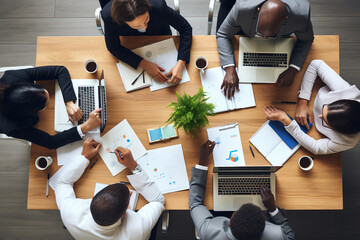 Above view of group of multi ethnic business people working in an office. Team of business people working on project in office, using laptop, writing notes at table with books, sharing learning tasks.